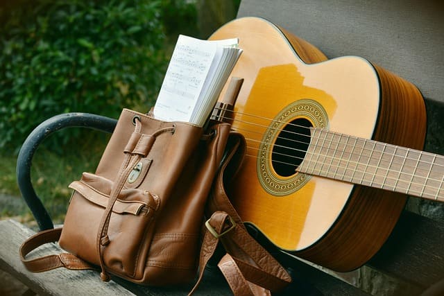 Klassische Akustikgitarre auf einer Parkbank mit Notenheft – ideal für alle, die Gitarre mit Noten lernen möchten.