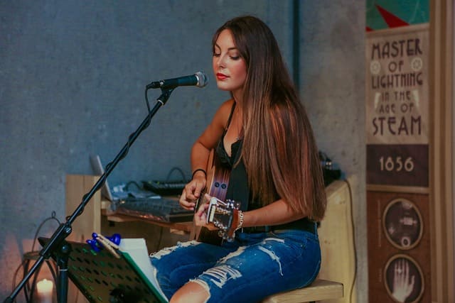 Junge Frau begleitet sich selbst auf der Akustikgitarre und singt live vor einem Mikrofon – perfektes Symbolbild für Gitarrenlieder für Anfänger.
