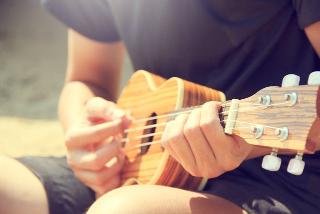 Person spielt eine Ukulele am Strand – Symbolbild für Ukulele für Anfänger.